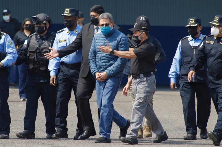Former Honduran President Juan Orlando Hernandez, center, is taken in handcuffs to a waiting aircraft as he is extradited to the United States.
