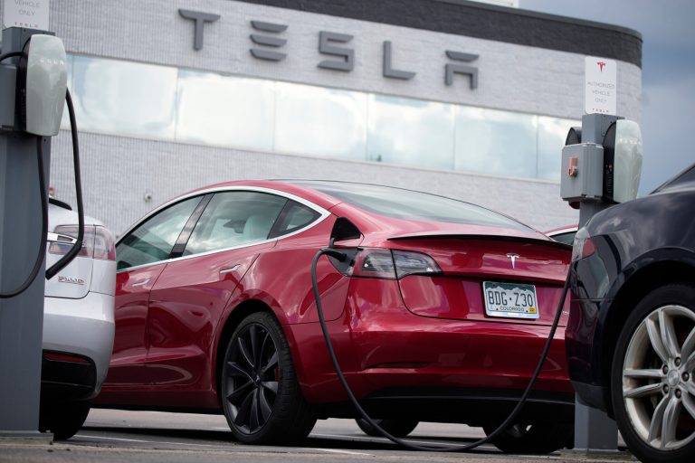 A Tesla Model 3 sedan is connected to a charger at a Tesla dealership on June 27, 2021, in Littleton, Colorado. 