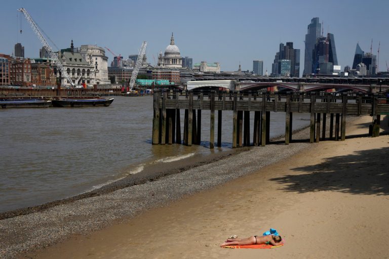 A woman sun bathes on the beach on the bank of the River Thames opposite St Pauls Cathedral in London, Friday, June 17, 2022.
