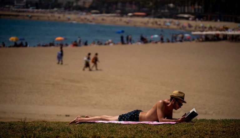 A man reads a book at a beach during a hot a sunny day in Barcelona, Spain, Monday, July 18, 2022.