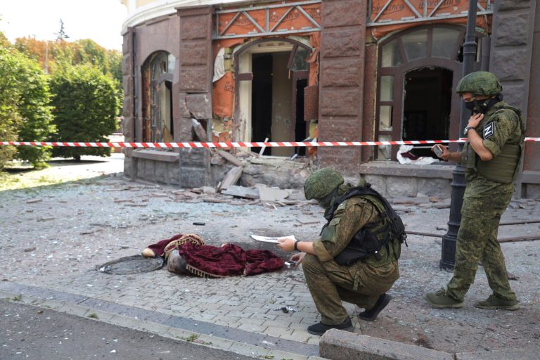 Investigative committee officers inspect an area of shelling as a lifeless body lies covered on the ground in Donetsk.