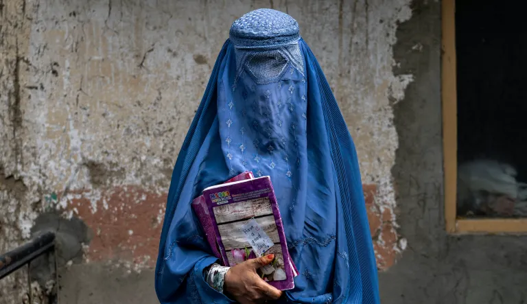 An Afghan woman leaves an underground school with books in her hand.
