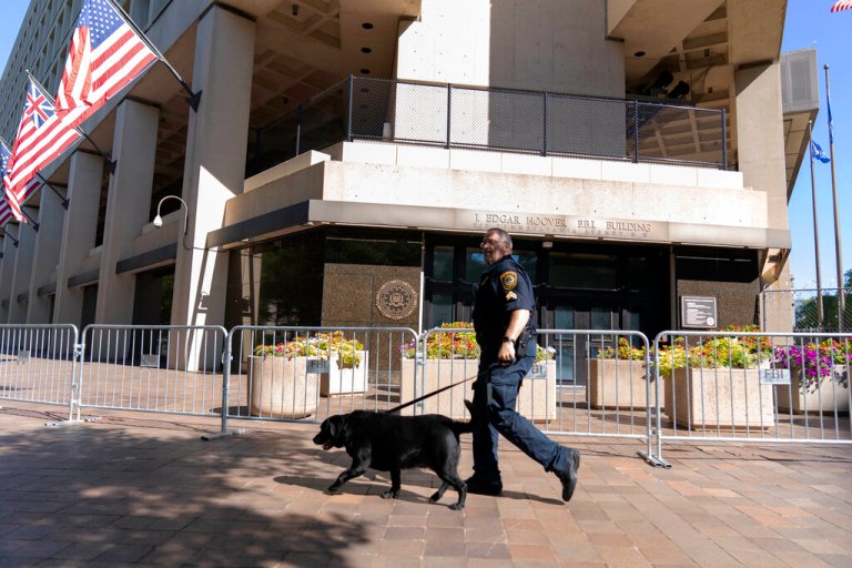 A Federal Bureau of Investigation police officer walks with his working dog outside the bureau's headquarters in Washington, Saturday, Aug. 13, 2022. 