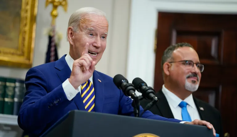 President Joe Biden speaks about student loan debt forgiveness in the Roosevelt Room of the White House, Wednesday, Aug. 24, 2022, in Washington. Education Secretary Miguel Cardona listens at right.