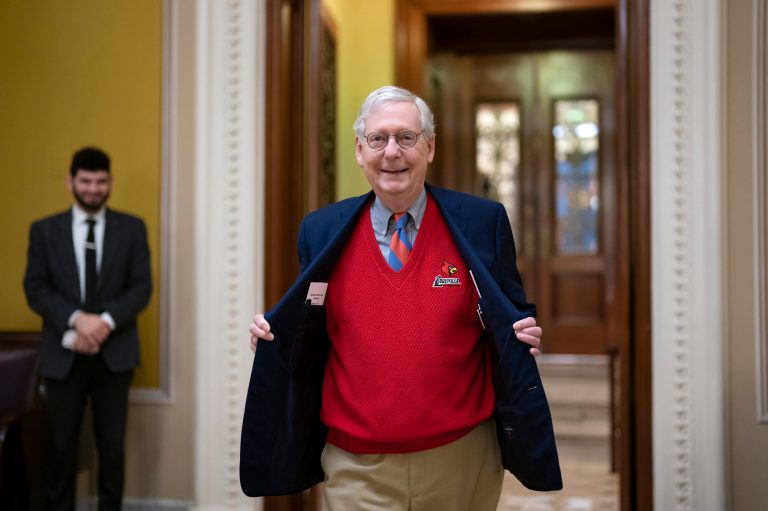 Senate Minority Leader Mitch McConnell, R-Ky., the top Republican, shows off his red University of Louisville sweater as he exits the chamber at the Capitol in Washington, early Thursday morning, Dec. 22, 2022. 
