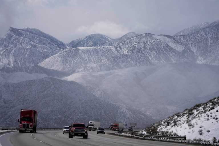 Vehicles make their way along the I-15 as clouds pass through the snow-covered mountains near Hesperia, California.