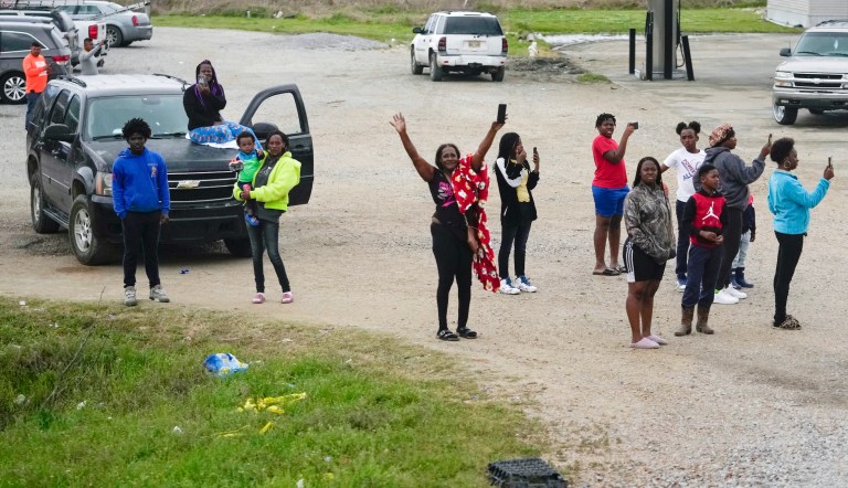 People wave and watch as the motorcade for President Joe Biden drives by en route to Rolling Fork, Mississippi, Friday, March 31, 2023. The president is traveling to meet with those affected by last week's massive storm. 