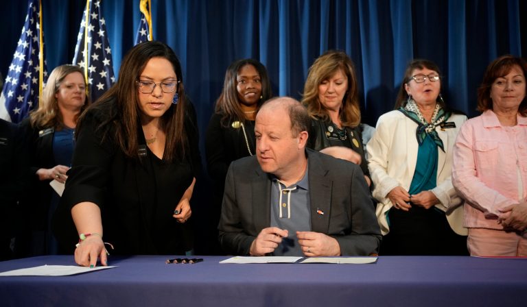 Colorado state Sen. Julie Gonzales, front left, confers with Gov. Jared Polis (D-CO) before he signs the first of three bills that enshrine protections for abortion.