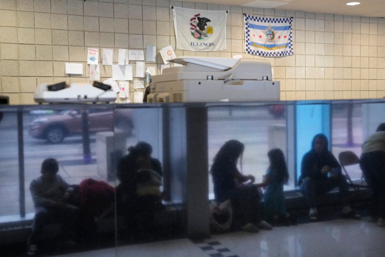 Immigrants from Venezuela are reflected in a marble wall while taking shelter at the Chicago Police Department's 16th District station on Monday, May 1, 2023. 