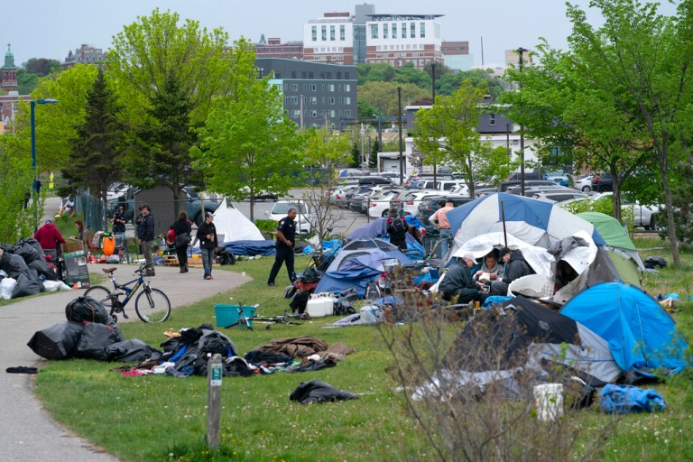 A police officer informs inhabitants of a homeless encampment to pack up before city workers arrive to clean up the area, Tuesday, May 16, 2023, in Portland, Maine.