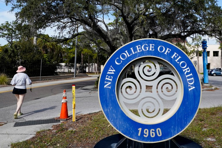 A student makes her way past the sign at New College of Florida, Jan. 20, 2023, in Sarasota, Florida. The New College of Florida trustees, dominated by conservatives appointed by Gov. Ron DeSantis (R-FL), chose a new mascot on Thursday, June 1, 2023, for the Sarasota school: the Mighty Banyans. The tree mascot will replace one that has been in use since 1997, which is the mathematical formulation of the null set. 