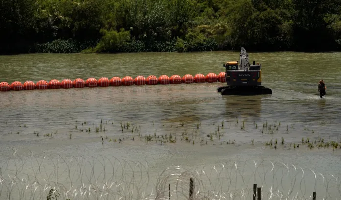 Workers deploy a string of large buoys to be used as a border barrier at the center of the Rio Grande.