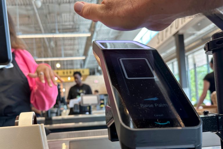 A customer pays for groceries using their palm handprint at an Amazon One device.