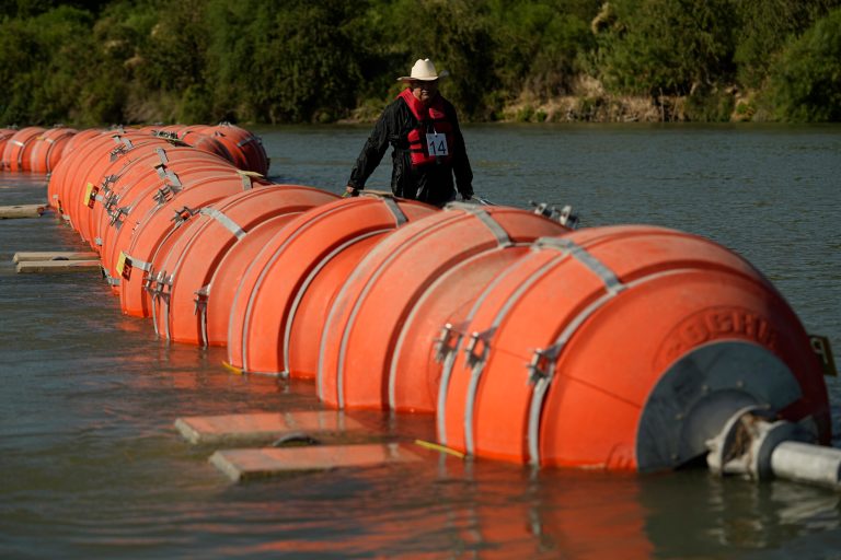 A kayaker walks past large buoys being used as a floating border barrier on the Rio Grande.