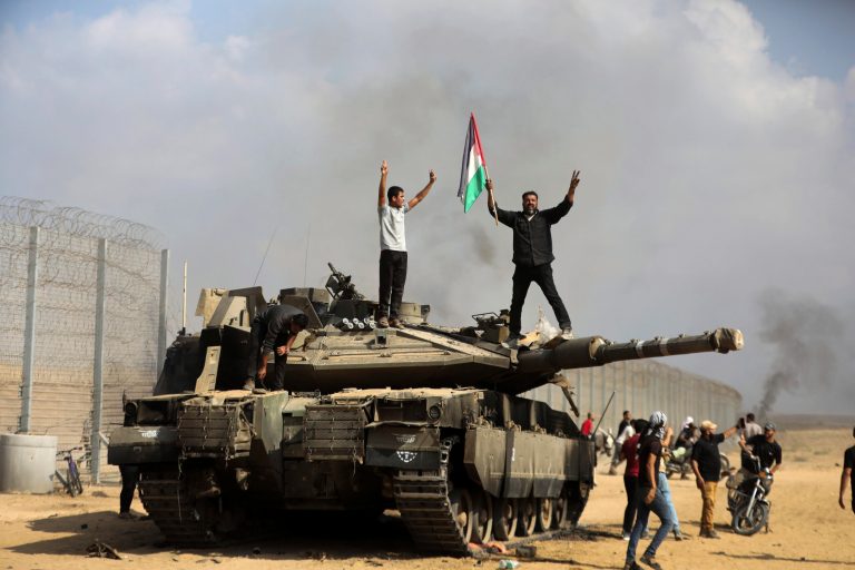 Palestinians wave their national flag and celebrate by a destroyed Israeli tank at the southern Gaza Strip fence east of Khan Younis Saturday, Oct. 7, 2023.