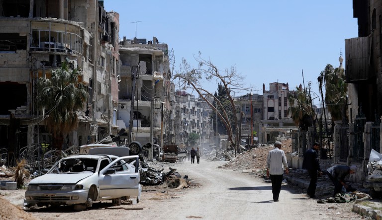 FILE - Syrians walk through destruction in the town of Douma, the site of a suspected chemical weapons attack, near Damascus, Syria, on April 16, 2018. (AP Photo/Hassan Ammar, File)