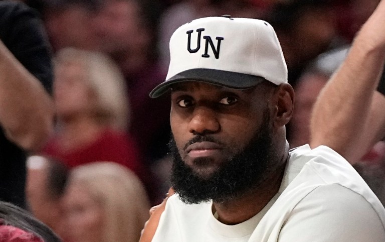LeBron James watches as his son, USC guard Bronny James, right, ties his shoes during the second half of an NCAA college basketball game against Long Beach State Sunday, Dec. 10, 2023, in Los Angeles.