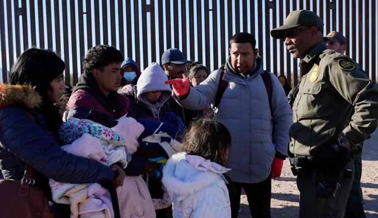Luiz Velazquez, second from right, from Zacatecas, Mexico, points to his family as he talks with a member of the U.S. Border Patrol as they join hundreds of migrants gathering along the border Tuesday, Dec. 5, 2023, in Lukeville, Arizona.