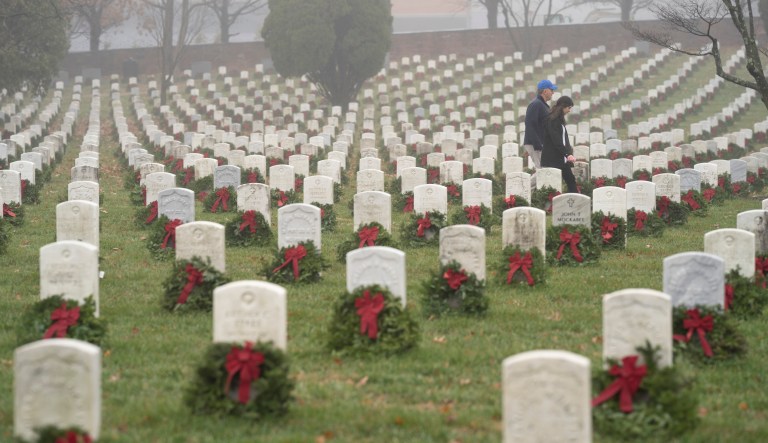 People walk among headstones with holiday wreaths in Arlington National Cemetery during Wreaths Across America Day in Arlington, Va., Saturday, Dec. 14, 2019.