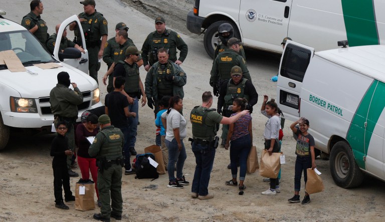 A girl waves to a young man watching from Mexican territory who said he was her cousin, as a group of Honduran asylum seekers is taken into custody by U.S. Border Patrol agents after the group crossed the U.S. border wall into San Diego, California, seen from Tijuana, Mexico, Monday, Dec. 10, 2018.