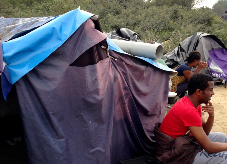 In this photo taken Sunday, Sept. 7, 2014, migrants sit by a tent at a makeshift camp in Calais, northern France. Migrants huddle in shanty-towns in Calais, gazing out at a tantalizingly narrow stretch of water toward Britain - the land they see as their Eldorado. They are pouring into the French port city at an ever-faster pace, overwhelming police with aggressive new tactics in their bid to cross the English Channel. (AP Photo/Elaine Ganley)