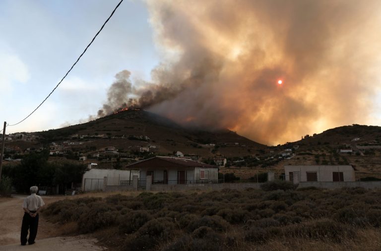 A local resident watches a fire burns a forest near the town of Keratea, 40 kilometers (25 miles) southeast of Athens on Saturday, July 12, 2014. At least one house has burned down and several others are in danger from a wildfire raging near Keratea. The fire broke out early Saturday afternoon in a forested area in the hills west of the city and has spread quickly, despite the efforts of more than 150 firefighters. (AP Photo/Thanassis Stavrakis)