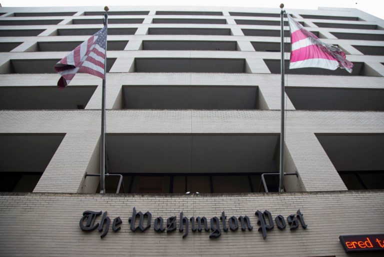 FILE - In this Aug. 6, 2013, file photo, an American flag, left, and a District of Columbia fly outside The Washington Post building in Washington. The longtime headquarters building of The Washington Post is being sold to a real estate development company for $159 million. Graham Holdings Co. is the former parent of The Washington Post newspaper. The company announced a deal Nov. 27, to sell the downtown Washington building to Carr Properties.  (AP Photo/Evan Vucci, File)