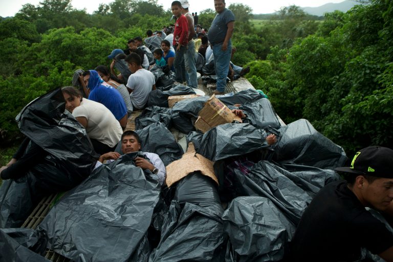 In this Friday, June 20, 2014 photo, Central American migrants use trash bags and cardboard to protect themselves from the rain as they wait atop a stuck freight train, outside Reforma de Pineda, Chiapas state, Mexico. The first leg of the long cross-country train journey, to Ixtepec in Oaxaca, typically takes 12-14 hours. On this occasion, the migrants had to endure alternate exposure to rain, cold, and heat for two full days, as the train suffered a minor derailment in a remote area halfway to Ixtepec. (AP Photo/Rebecca Blackwell)
