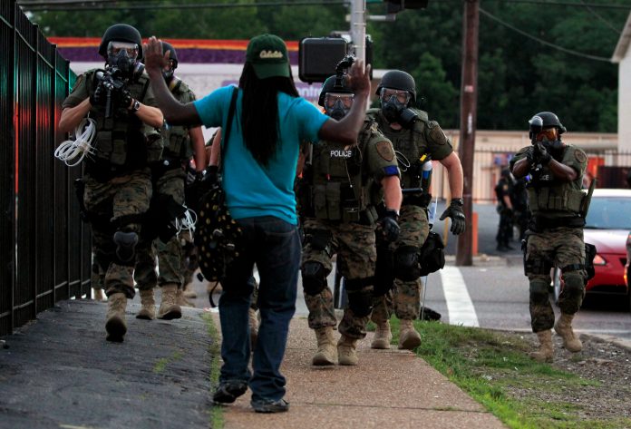 Police wearing riot gear walk toward a man with his hands raised Monday, Aug. 11, 2014, in Ferguson, Mo. (AP Photo/Jeff Roberson, File)