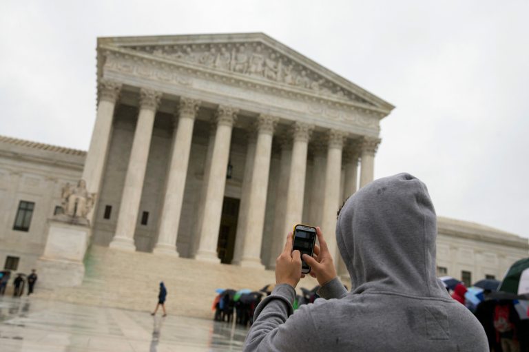 FILE - This April 29, 2014 file photo shows a Supreme Court visitor using his cellphone to take a photo of the court in Washington. A unanimous Supreme Court says police may not generally search the cellphones of people they arrest without first getting search warrants. The justices say cellphones are powerful devices unlike anything else police may find on someone they arrest.  (AP Photo, File)
