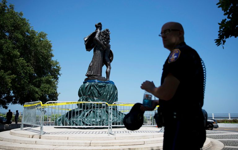 A police officer stands next to a statue memorializing the Confederacy as it's taped off and its base covered by a tarp after police said someone spray-painted the message 