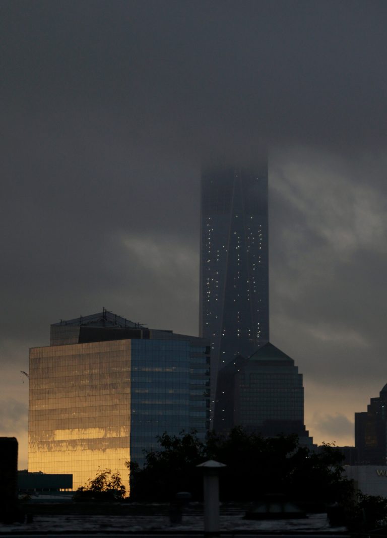 Storm clouds obscure the top of 1 World Trade Center seen from The Heights neighborhood of Jersey City, N.J., at sunrise, Thursday, Sept. 11, 2014. Thirteen years after 9/11 forever changed the New York skyline, officials say developments at the World Trade Center are on track and on budget. (AP Photo/Julio Cortez)