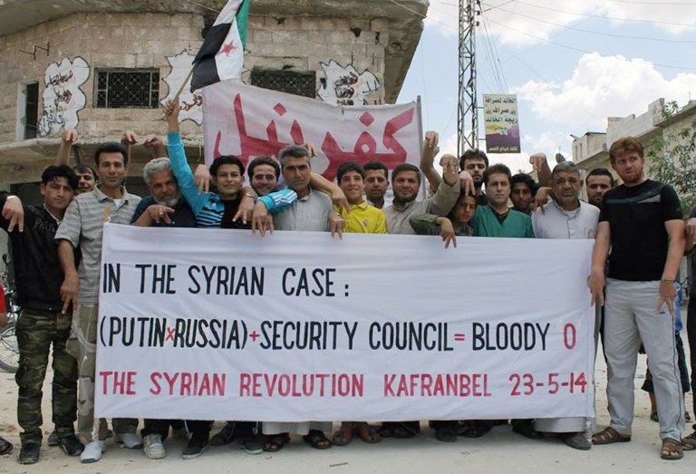 This photo provided by an anti-Bashar Assad activist group Edlib News Network (ENN), which has been authenticated based on its contents and other AP reporting, show anti-Syrian government protesters carrying a banner and a Syrian revolution flag during a demonstration in Kafr Nabil town, Idlib province, northern Syria, Friday, May 23, 2014. (AP Photo/Edlib News Network ENN)