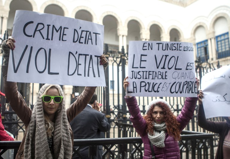 Tunisian women demonstrate outside a Tunis courthouse where three police officers face charges of rape of a 27-year-old woman, Monday, March 31, 2014. The 27-year-old woman says three police officers stopped her in a car in September, and one of them held her fiance back while the other two raped her.  The police officers deny wrongdoing, and allege the couple had been engaged in 