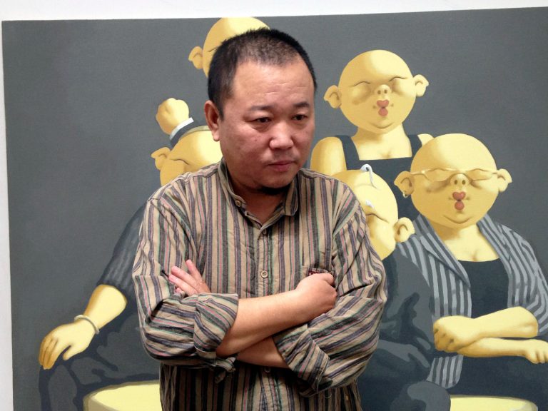 In this photo taken Sept. 20, 2014, Chinese artist Li Dapeng talks to reporters in front of one of his works depicting a typical Chinese scene featuring figures with grotesque pig heads at his studio in the Songzhuang art district in eastern Beijing, China. Artists in Songzhuang have long enjoyed rare creative freedoms by keeping their art and conversation mostly away from the public, but police arrested 13 people who work or live in the district in October after they posted online pictures and commentary support pro-democracy demonstrators in Hong Kong.(AP Photo/Jack Chang)
