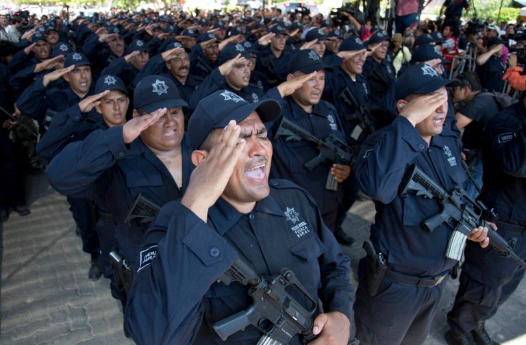 FILE - In this May 10, 2014 file photo, former members of self-defense groups wear their newly-issued rural police uniforms, and salute during the start of a ceremony in Tepalcatepec, Mexico. The federal government acknowledges that the new rural police force in Michoacan state is being given uniforms and powerful weapons with minimal background checks and virtually no training. (AP Photo/Eduardo Verdugo, File)