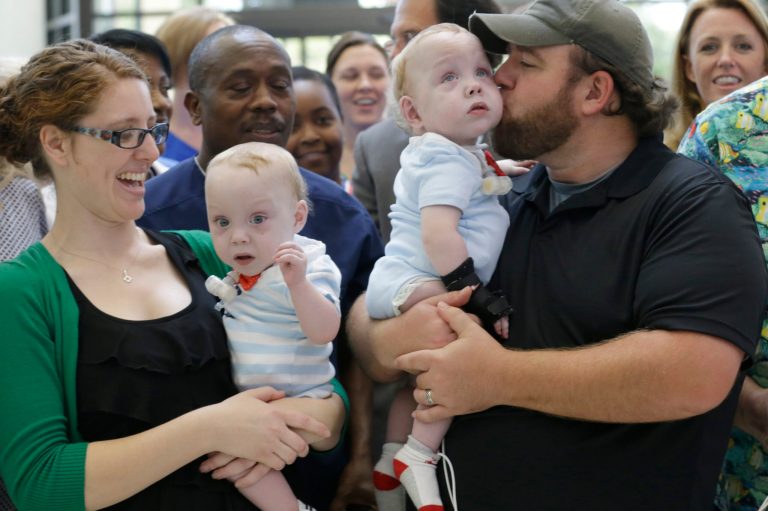 Emmett Ezell, second from right, is kissed by his father, Dave, as his brother, Owen, is held by his mother, Jenni, as they prepare for a group photo with caregivers at Medical City Children's Hospital in Dallas on Thursday, July 24, 2014.  The formerly conjoined twin boys returned to the hospital where they were surgically separated to celebrate their first birthday with those who helped care for them. (AP Photo)
