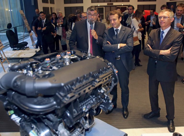 French Economy and Industry Minister Emmanuel Macron, center, listens to the explanations of PSA Peugeot research director Gilles Le Borgne, left, as they watch the EB turbo pure tech engine during his visit to the PSA Peugeot Citroen headquarters in Paris, Tuesday Sept. 30, 2014. Watching at right is PSA Peugeot Citroen chairman Carlos Tavares.  (AP Photo/Remy de la Mauviniere)