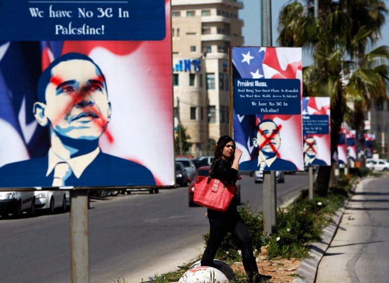 FILE-- In this Friday, March. 15, 2013 file photo, a Palestinian woman walks past vandalized posters showing US President Barack Obama, in the West Bank city of Ramallah. When he visits the region next week President Obama will find a disillusioned Palestinian public, skeptical about his commitment to promoting Mideast peace, and who accuse him of unfairly favoring Israel. (AP Photo/Majdi Mohammed, File)