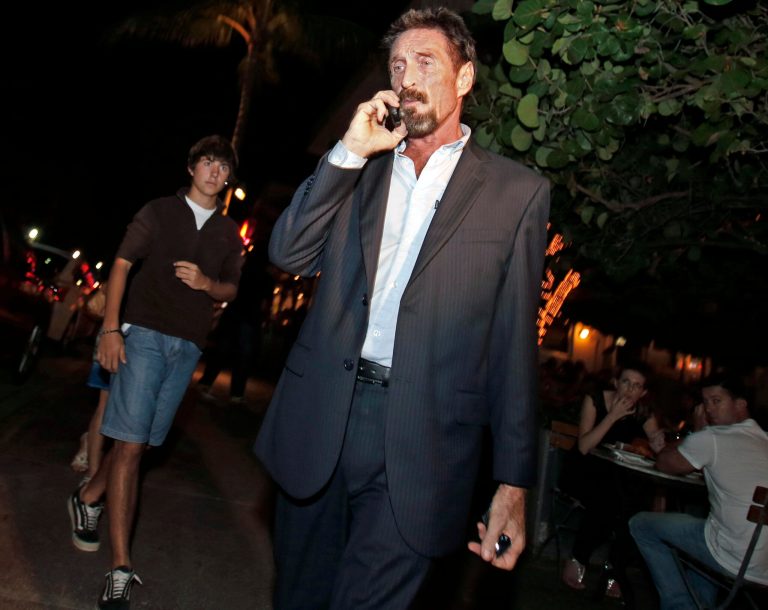   Anti-virus software founder John McAfee talks on his mobile phone as he walks on Ocean Drive in the South Beach area of Miami Beach, Fla., on his way to dinner Wednesday, Dec 12, 2012. McAfee arrived in the U.S. on Wednesday night after being deported from Guatemala, where he had sought refuge to evade police questioning in the killing of a man in neighboring Belize.(AP Photo/Alan Diaz)  
