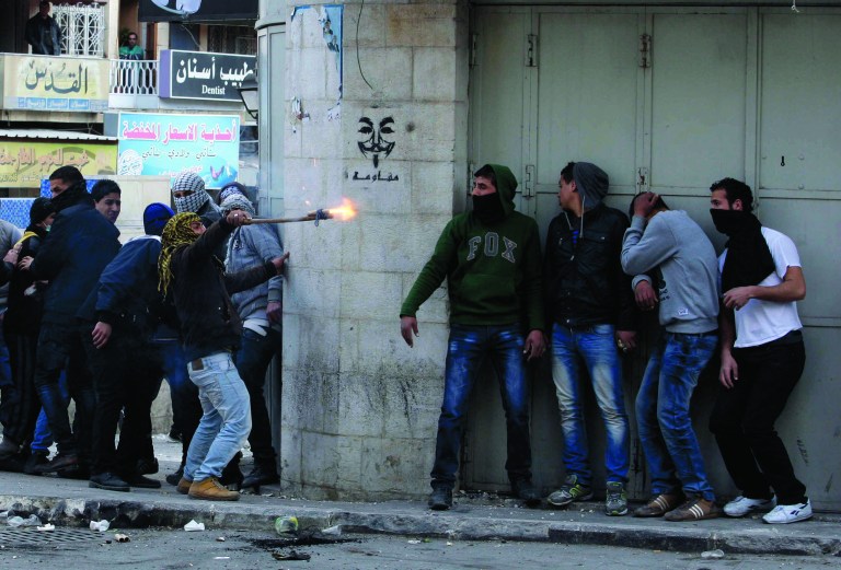 Palestinians take cover during clashes with Israeli troops in the West Bank city of Hebron, following the death of Arafat Jaradat, a Palestinian prisoner held in an Israeli jail, Sunday, Feb. 24, 2013. The death of a 30-year-old Palestinian after interrogation by Israel's Shin Bet security service stokes new West Bank clashes, along with Israeli fears of a third Palestinian uprising. (AP Photo/Nasser Shiyoukhi)