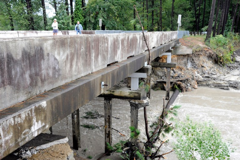In this Monday, Oct. 5, 2015 file photo, Residents of a lakeside neighborhood walk across Overcreek Bridge by the remains of a failed dam in Columbia, S.C. Officials say the structure beneath a road collapsed Monday afternoon following days of heavy rain, nearly emptying a lake in a few minutes. (AP Photo/Jay Reeves, File)