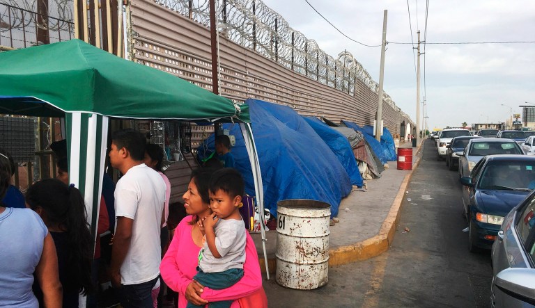 In this May 5, 2019 photo, migrants walk between tents, left, and cars waiting to cross the border in San Luis Rio Colorado, Mexico, and Arizona. The tent slots are for families about to be called, allowing them to be ready on a momentâs notice.