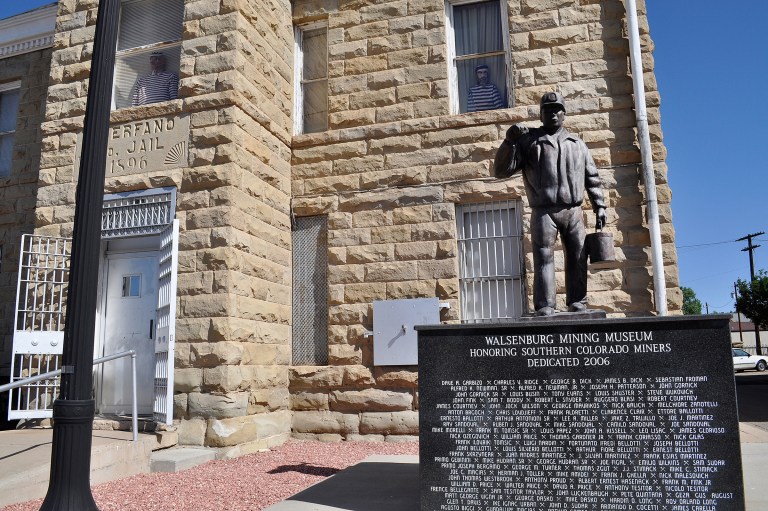 A bronze miner carrying a pale with a pick over his shoulder stands on top of the monument with the names of hundreds of miners in front of the Walsenburg Mining Museum on June 19, 2014 in Walsenburg, Colo. Figures of prisoners peak out windows of the building that was once a jail. (AP Photo/The Pueblo Chieftain, John Jaques)