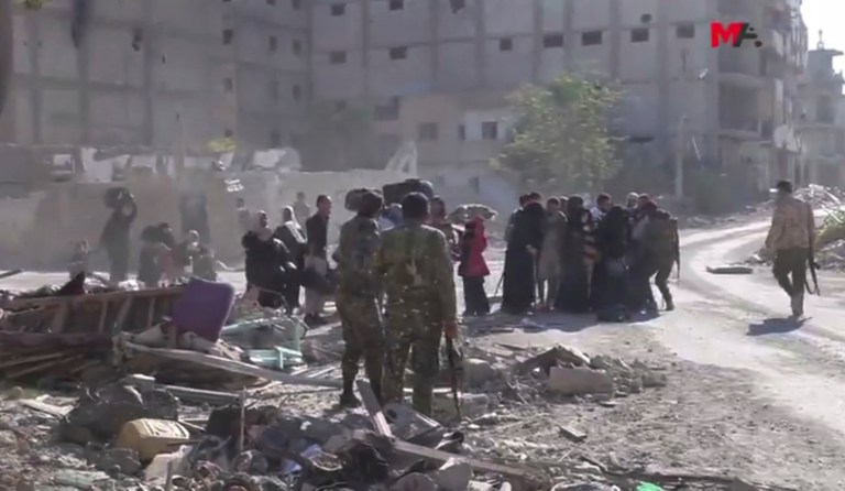 This frame grab from a video provided on Friday, Oct. 13, 2017 by Turkey-based Kurdish Mezopotamya agency media outlet shows U.S.-backed Syrian Democratic Forces fighters, standing near Syrian civilians who fled from the areas that still controlled by Islamic State militants in Raqqa, Syria. (Mezopotamya Agency, via AP)