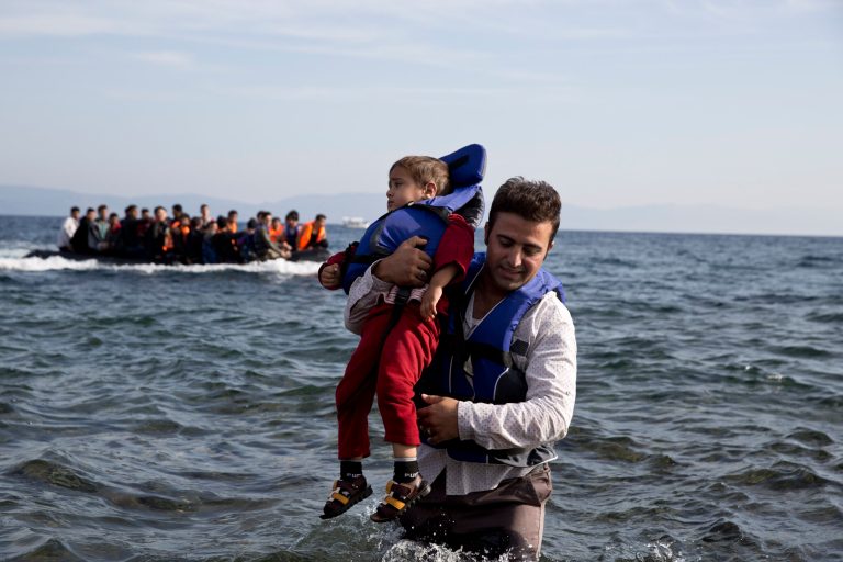 A Syrian refugee carries his child after they arrived from Turkey to the shores of the Greek island of Lesbos, on an inflatable dinghy, with another boat in the background, Saturday Sept. 26, 2015. (AP Photo/Petros Giannakouris)