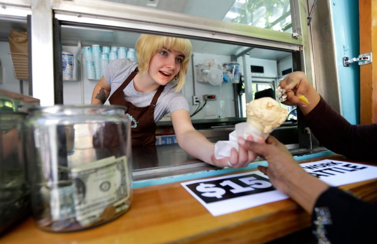 Caitlyn Faircloth, a worker with Molly Moon's Homemade Ice Cream, hands out free ice cream next to a tip jar, Monday, June 2, 2014, at a rally celebrating the passage of a $15 minimum wage measure outside Seattle City Hall in Seattle. The Seattle City Council passed a $15 minimum wage measure, Monday, but not until after debate over how long businesses will have to phase in the measure, and how tips, benefits, and other forms of compensation will be considered. (AP Photo/Ted S. Warren)