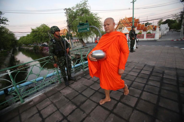A Buddhist monk walks past soldiers in Bangkok, Thailand, Friday, May 23, 2014 after Thai military staged a coup. Thailand's new military junta has announced that it has suspended the country's constitution. Without firing a shot, Thailand's powerful military seized control of this volatile Southeast Asian nation Thursday, suspending the constitution and detaining Cabinet ministers in a risky bid to end half a year of political upheaval that many fear will only deepen the nation's crisis. (AP Photo/Sakchai Lalit)