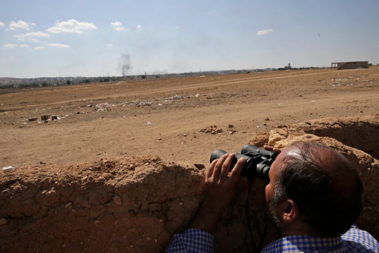 A Turkish Kurd uses binoculars in Mursitpinar, on the outskirts of Suruc, on the Turkey-Syria border, as he watches the intensified fighting between militants of the Islamic State group and Kurdish forces in Kobani, Syria, background, Wednesday, Oct. 8 Oct. 7, 2014. Kobani, also known as Ayn Arab and its surrounding areas have been under attack since mid-September, with militants capturing dozens of nearby Kurdish villages. (AP Photo/Lefteris Pitarakis)