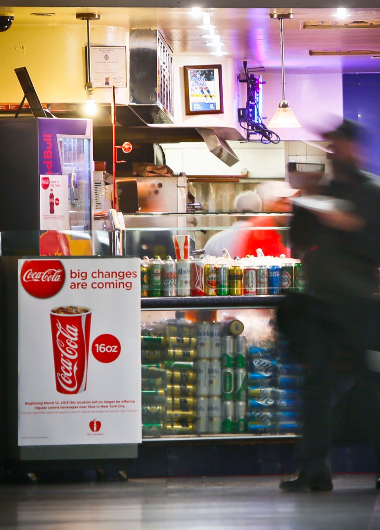 FILE - In this March 8, 2013 file photo, a Coca-Cola poster about the city's anticipated beverage ban is displayed at a pizza shop at New York's Penn Station. New York City's groundbreaking limit on the size of sugar-laden drinks has been struck down by a judge shortly before it was set to take effect. The restriction was supposed to start Tuesday, March 12, 2013. The rule prohibits selling non-diet soda and some other sugary beverages in containers bigger than 16 ounces. It applies at places ranging from pizzerias to sports stadiums, though not at supermarkets or convenience stores. (AP Photo/Bebeto Matthews)
